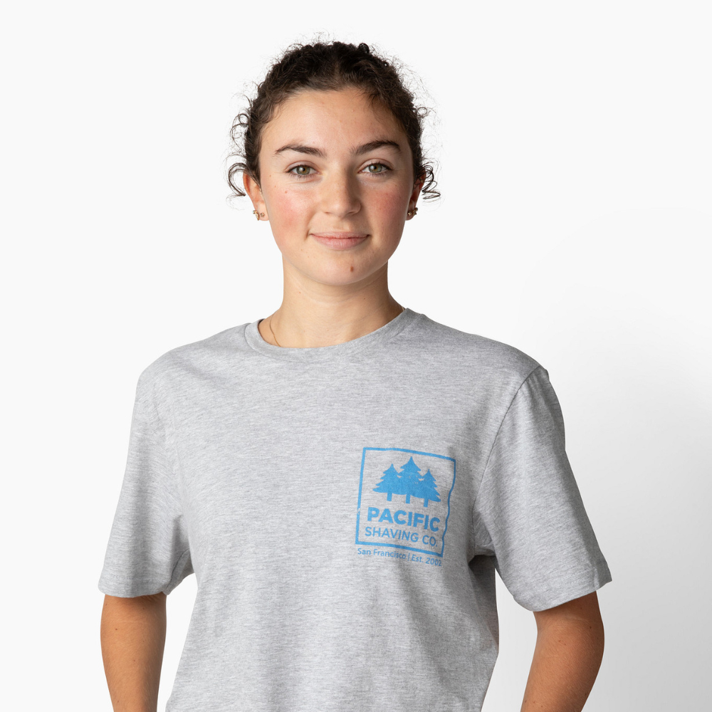 Woman wearing a gray t-shirt with a Pacific Shaving Company logo on a white background.