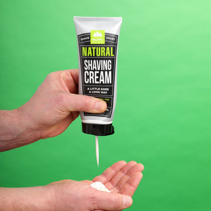 Hand holding a tube of natural shaving cream against a green background