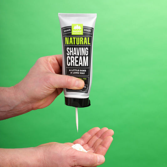 Hand holding a tube of natural shaving cream against a green background