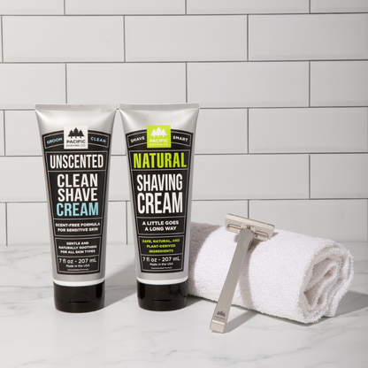Two tubes of Shave Cream with a razor and towel on a tiled bathroom counter.
