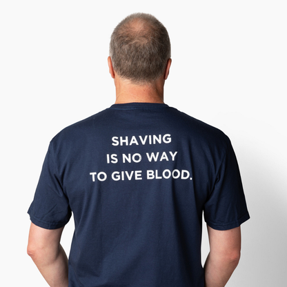 Man wearing a navy blue t-shirt with text on the back that says "Shaving is no way to give blood" against a white background
