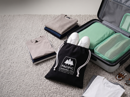Packing process with clothes, shoes, and a Pacific Shaving Company Travel Bag.